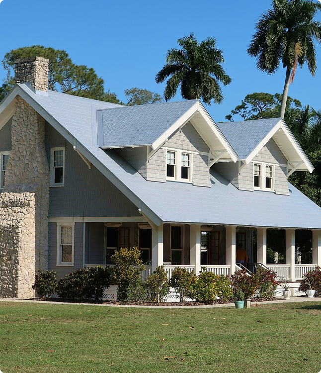 Florida home with gray siding and a light blue roof, showcasing meticulous workmanship and a welcoming porch surrounded by lush greenery.