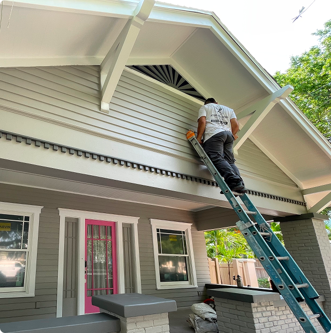 Painter on ladder applying a fresh coat of paint to the exterior of a house in a humid Florida climate, showcasing attention to detail and quality craftsmanship.