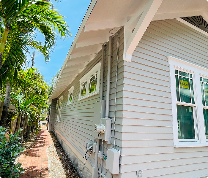 Exterior of a freshly painted Florida home, showcasing light gray siding, new windows, and a clean walkway lined with tropical plants, emphasizing the importance of proper surface preparation in exterior painting services.