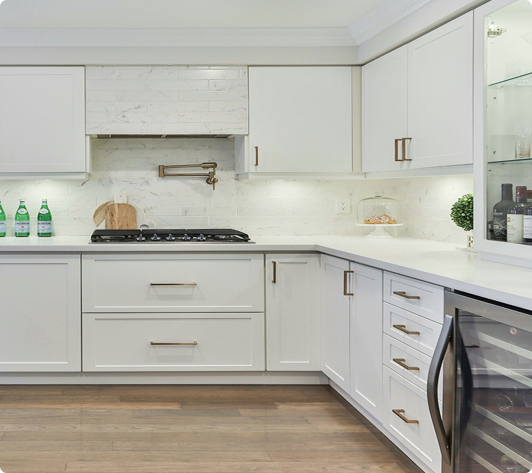Modern kitchen featuring white cabinets with gold hardware, marble backsplash, gas stove, and wine cooler, emphasizing a clean and stylish design suitable for cabinet painting services.