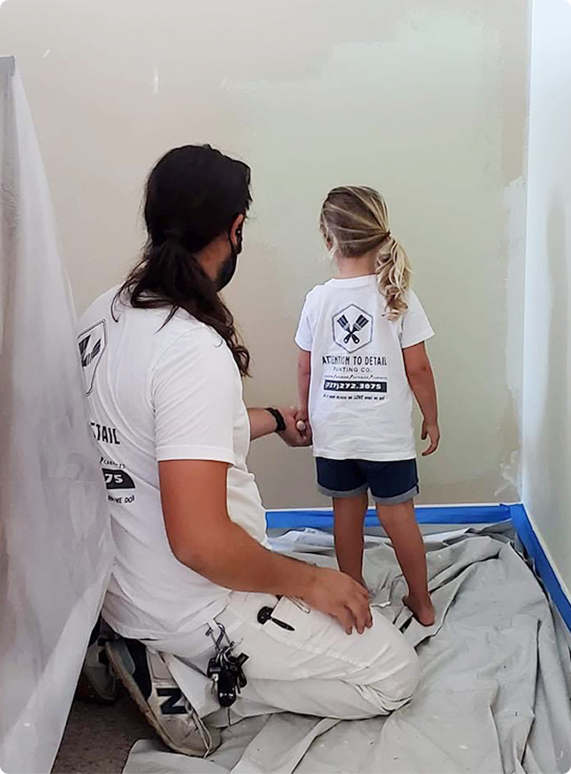 Painter and child in matching "Attention to Detail Painting" shirts, engaged in home painting project, showcasing local craftsmanship and family-oriented values in Pinellas County.