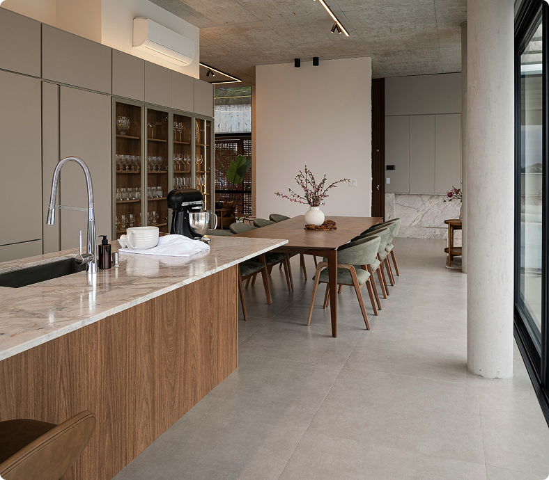 Modern kitchen with wood and marble countertops, sleek cabinetry, dining table with green chairs, and natural light.