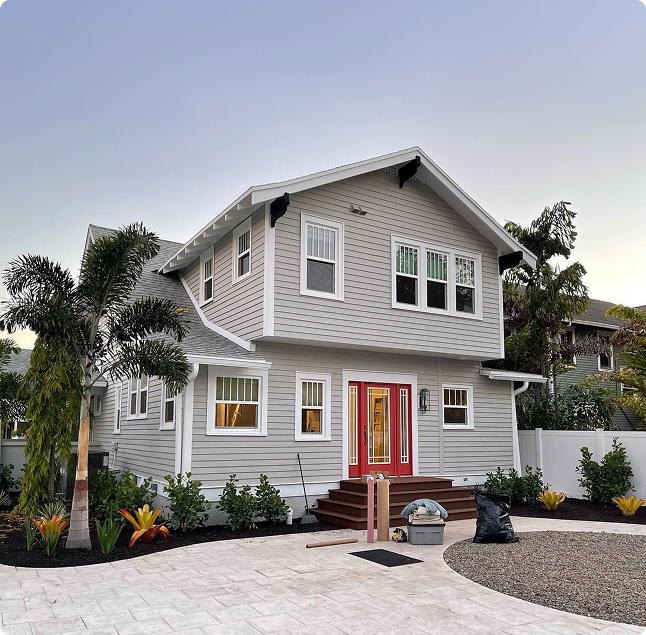 Coastal home in Madeira Beach with gray siding, red front door, and lush landscaping, highlighting professional painting services for waterfront properties.