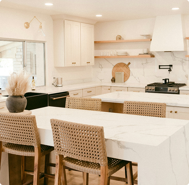 Modern kitchen featuring a marble island, woven bar stools, white cabinetry, and open shelving, showcasing a stylish and functional space for cabinet refinishing and interior painting.
