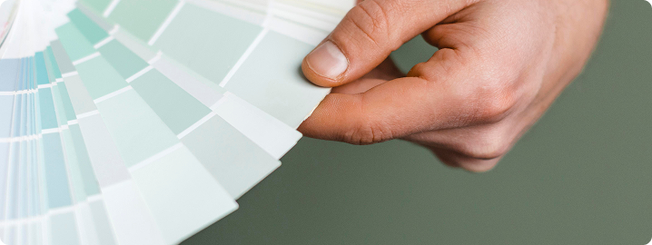 Hand holding a fan of coastal color paint swatches, showcasing light greens and whites, relevant to color design for beach aesthetics in Pinellas County.
