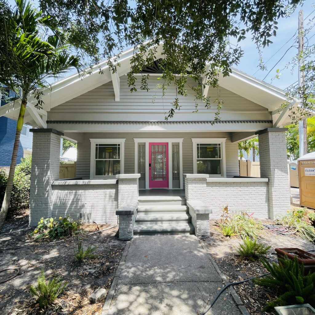 Front view of a freshly painted house with a vibrant pink door, showcasing meticulous craftsmanship and landscaping, highlighting Attention to Detail Painting's services in Pinellas County.