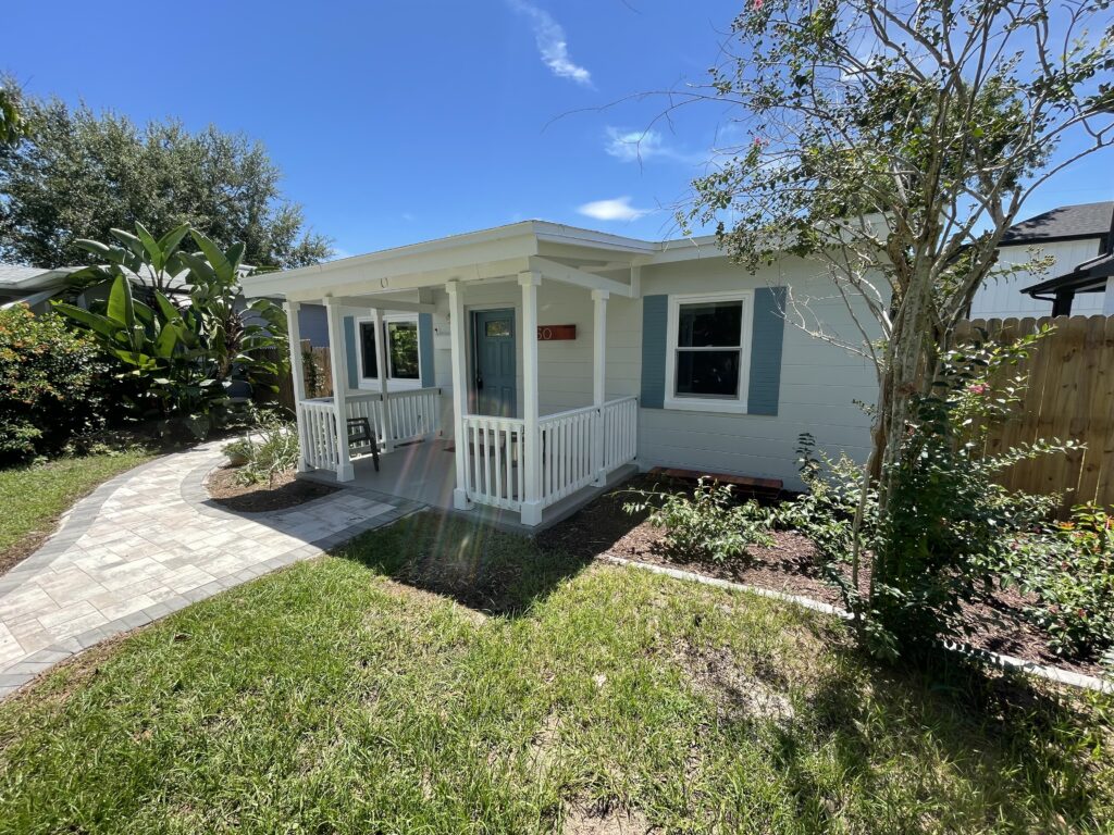 Exterior view of a painted house with a welcoming porch, surrounded by lush greenery and a stone pathway, reflecting quality painting services offered by Attention to Detail Painting in Pinellas County.