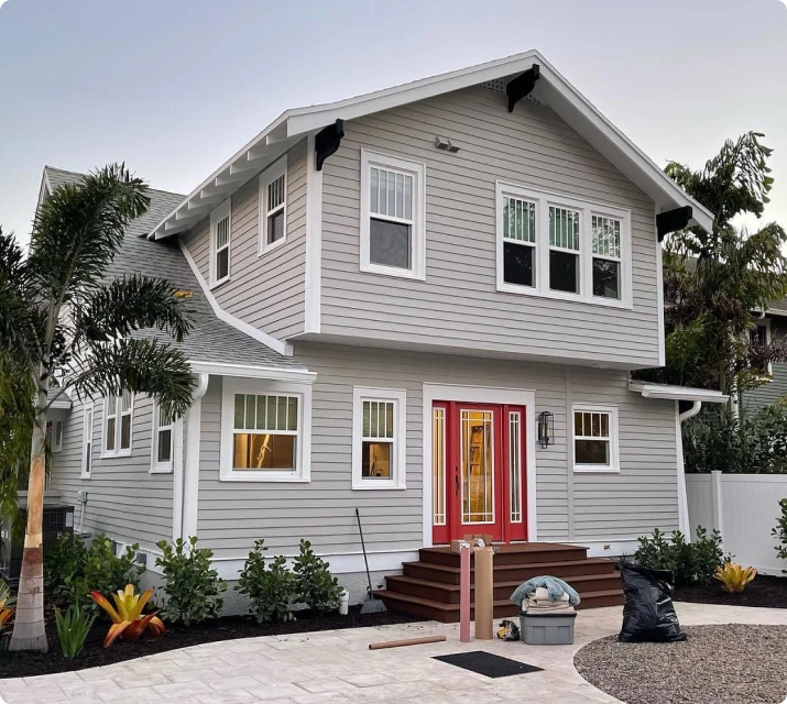 Two-story gray house with a red front door and tropical landscaping