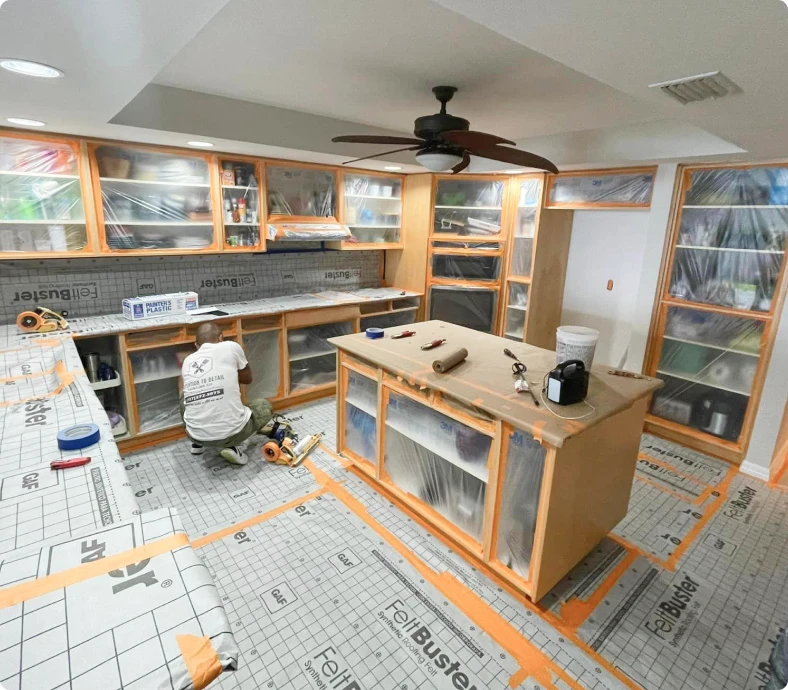 Kitchen cabinets wrapped in plastic with the floor covered during painting prep