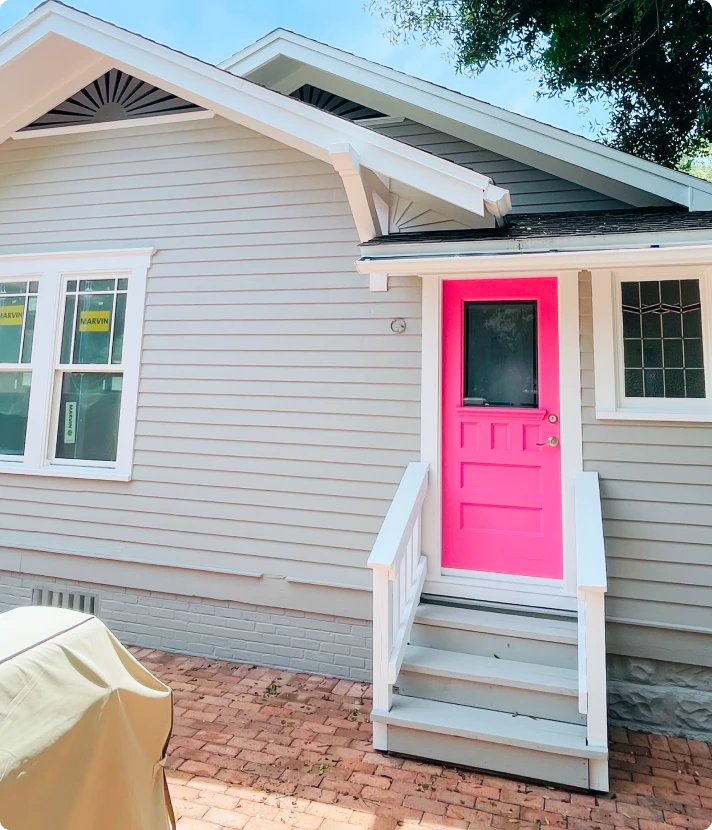 Bright pink front door on a gray cottage with white entry steps